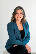 headshot of woman sitting down and smiling at camera with a grey background.